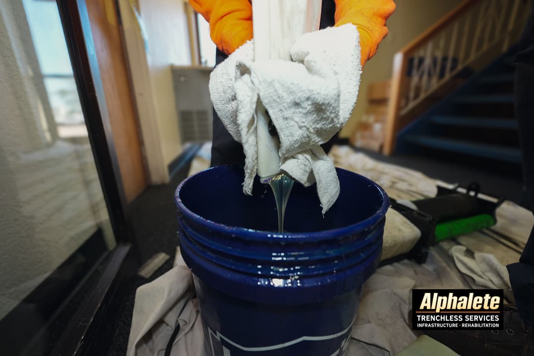 Worker using a towel to extract liquid into a blue bucket for trenchless service.