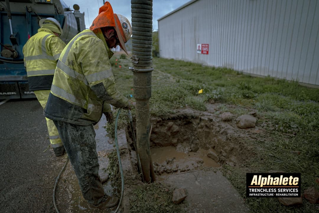 Workers operating trenchless technology equipment for infrastructure repair in wet conditions.