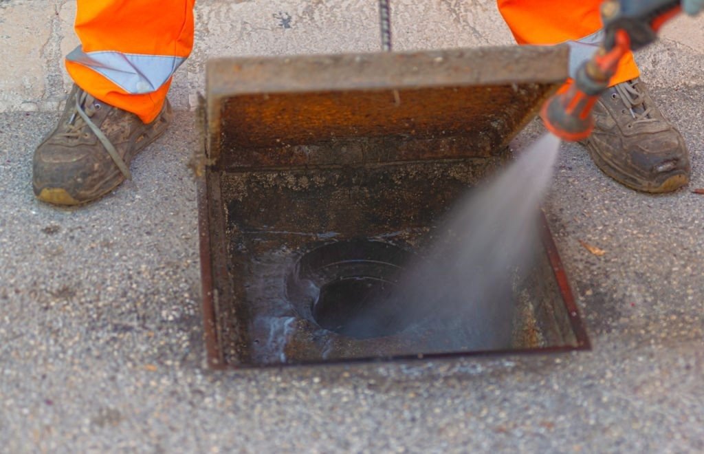 Technician using high-pressure hydro jetting equipment to clean a sewer access point in Louviers.