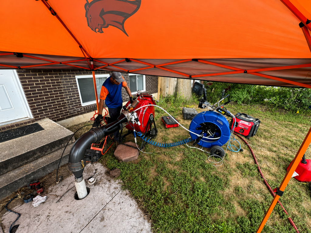 Technician operating trenchless sewer pipe repair equipment outside a residential property